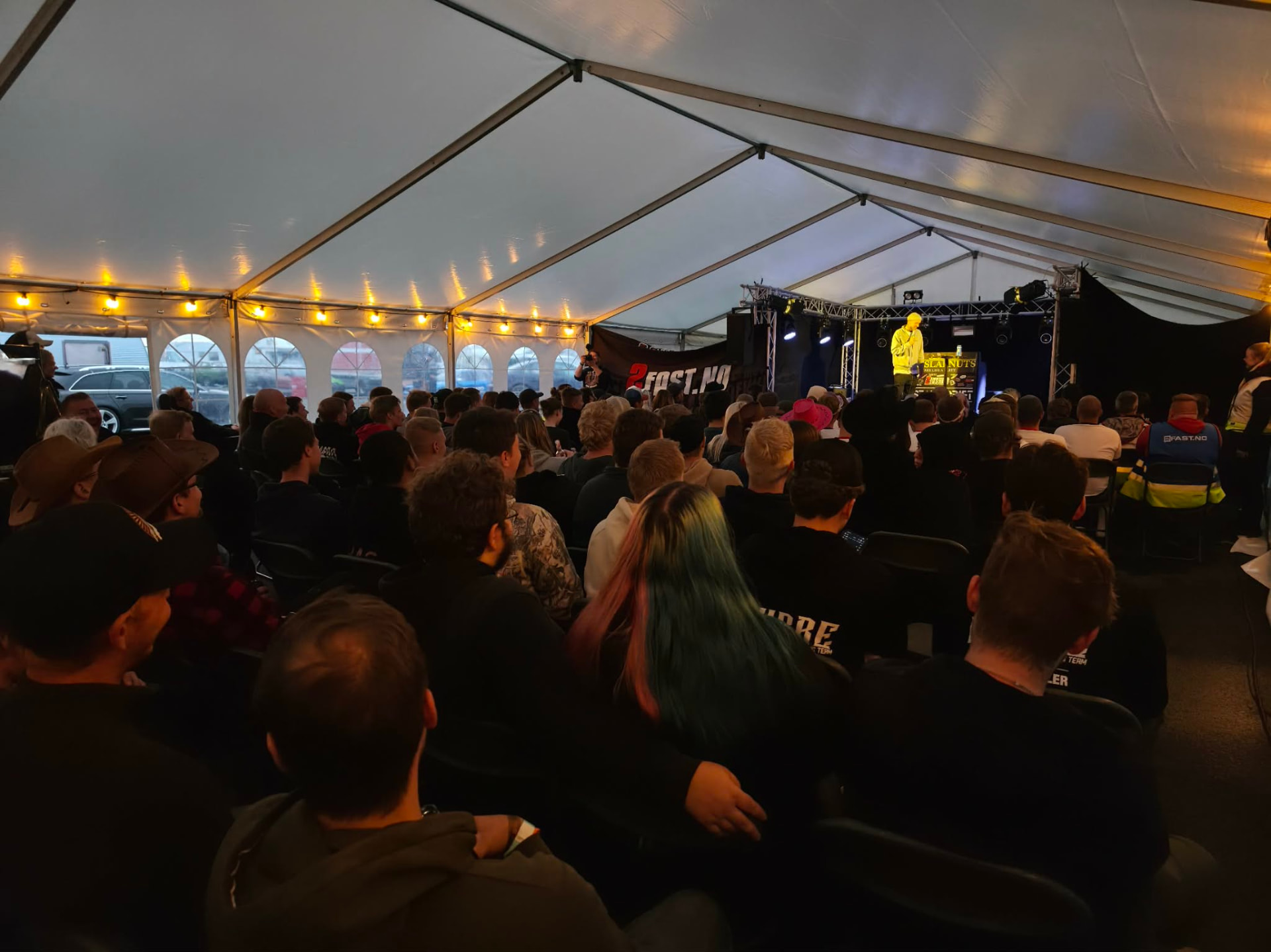 Fullsatt festtelt med komiker i gul jakke på scenen