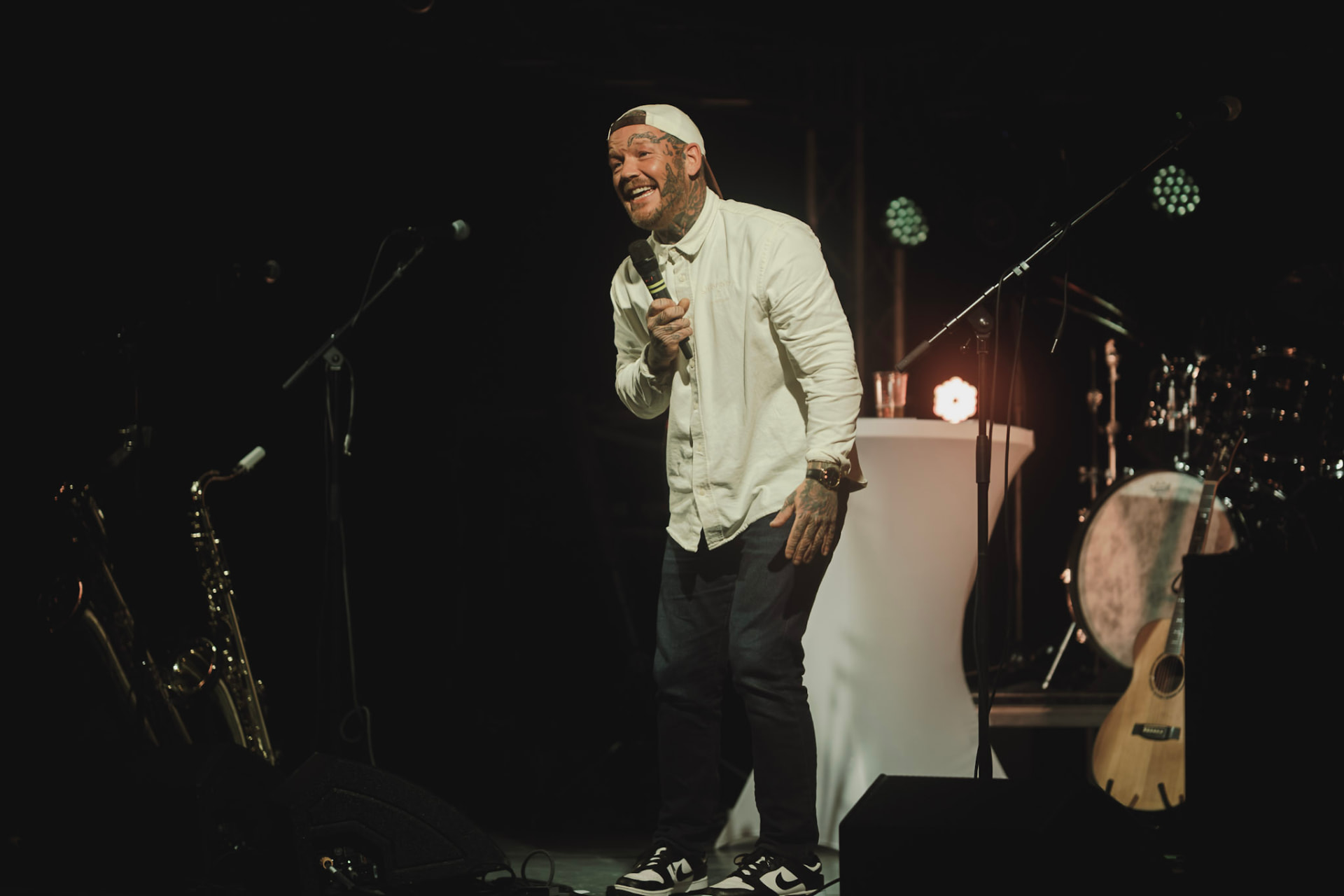 Komiker med caps og mikrofon smiler på scenen